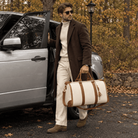 Homme portant un sac de voyage blanc et marron RAVELEE à côté d’un SUV en automne